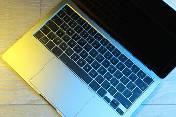 Fototapeta premium Stylish modern laptop in neon lights on wooden table, top view