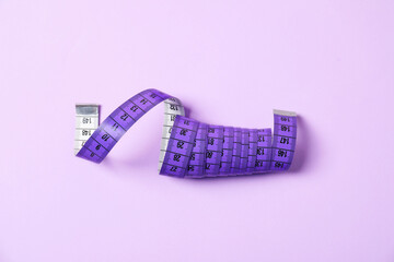 One measuring tape on violet background, top view