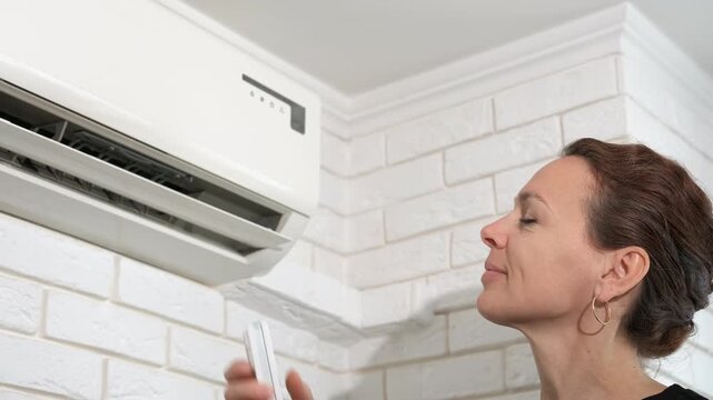 Female switching controller of conditioner. A view of resting female with switch the air conditioner on the wall in the room