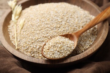 Oat bran in bowl, spoon and spike on wooden table, closeup