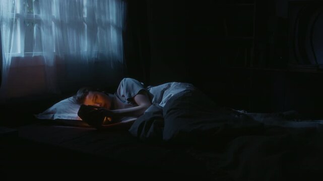 Wide angle shot of young adult woman checking stressful content on social media lying in bed during late night while procrastinating sleep