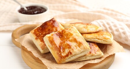 Tasty puff pastries and jam on white wooden table, closeup
