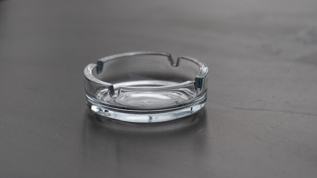 Transparent glass ashtray on gray surface with copy space