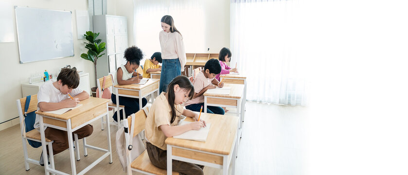 Pupil students with caucasian teacher in classroom at elementary school. Student boy study in primary school. Children writing notes in classroom. Education knowledge, teamwork concept banner