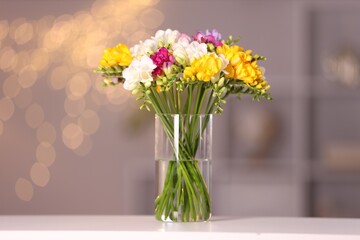 Obraz premium Bouquet of beautiful freesia flowers in vase on white table against blurred background