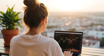 Fototapeta premium Woman analyses stock chart on laptop outdoors at sunset, with plant in a pot