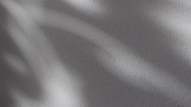 Rough gray plaster wall with soft sunlight spots and shadows. Minimal textured background with copy space, ideal for interior, design, and natural light concepts.