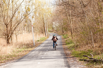 Obraz premium Boy riding bicycle along long forest cycling path in early spring