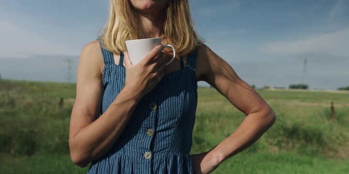 Woman holding a cup of coffee in a sunny countryside field