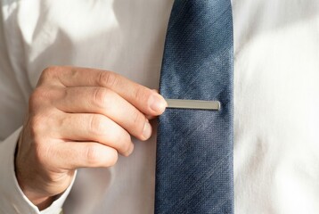 Man in a white shirt attaching a sleek silver tie clip to his dark blue textured necktie