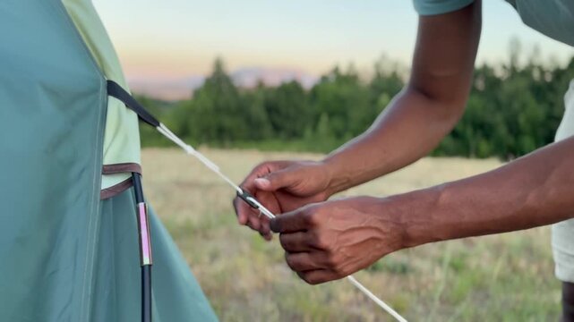 Detailed View of Hands Tensioning Ropes on a Modern Tent