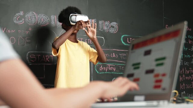 Closeup of school girl hand coding program while african student using VR interact with metaworld. Smart boy wearing virtual reality glasses and playing video games at innovative class. Edification