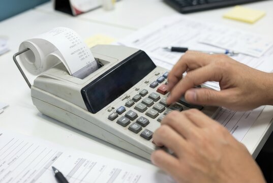 Accountant hands rapidly typing numbers on the keypad of a desktop printing calculator with a paper tape roll