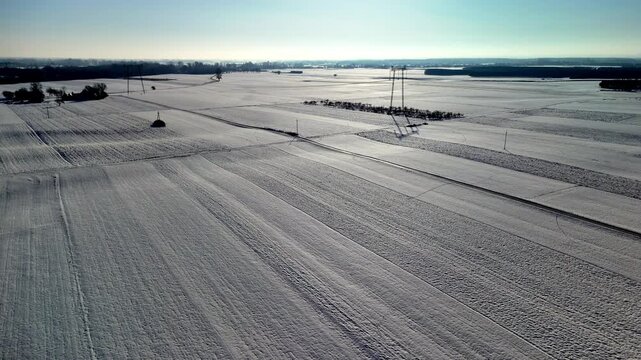 Aerial drone shot flying above wide snow covered farmland with distant horizon and winter landscape. Camera moves forward across frozen agricultural fields creating calm rural scenery.