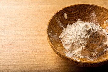 Fine powder ingredient in a rustic wooden bowl on wooden table with copy space, baking and cooking background, natural food texture, pantry staple, minimalist kitchen still life.