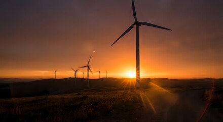 Obraz premium Wind turbines generating renewable energy at sunset with dramatic orange sky and sunburst over rural landscape for sustainable power and environmental concepts.