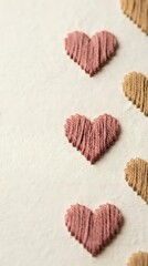 Fototapeta premium Handmade embroidered hearts in pink and beige thread on cream fabric background for Valentine's Day crafts and romantic textile projects.