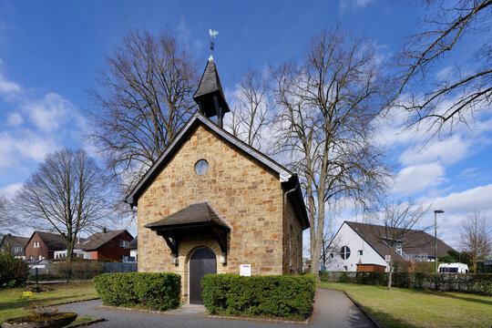 Exterior view of the small St. Roch chapel in Overath. Historic quarrystone building with a small bell tower and weather vane under a spring sky