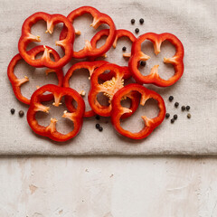 Macro Top View of Fresh Red Bell Pepper Rings and Black Peppercorns on Neutral Plaster Background with Copy Space