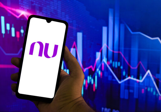 Nubank logo on a smartphone screen with financial market charts in the background. Nubank is a Brazilian digital bank considered the largest in Latin America.