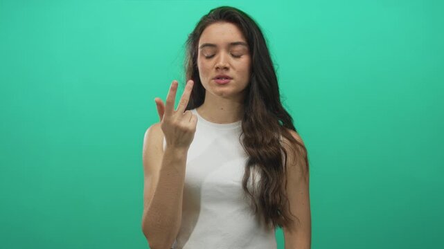 Woman counting fingers in green studio holds index finger up with furrowed brow while looking down at hand; concentration.