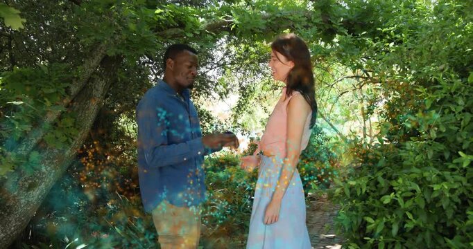 Couple walking along leafy garden path, colorful powder swirling, man kneeling proposing ring