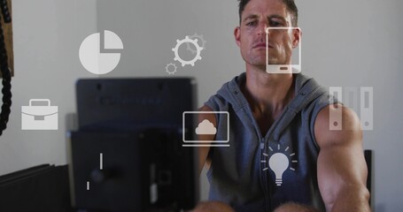 Rowing man wearing sleeveless hoodie using rower facing blurred monitor in home gym with icons © vectorfusionart