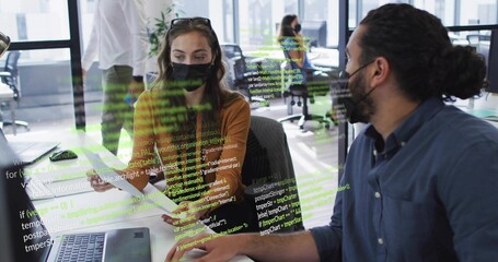 Working duo wearing masks leaning over laptop and papers in open office showing code overlay © vectorfusionart