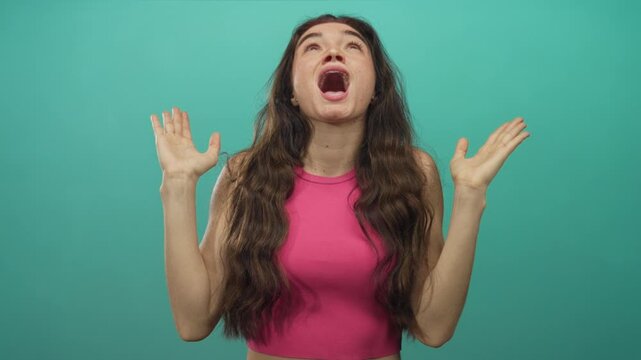 Young hispanic woman in pink top raises bare arms, tilts head back and smiles with eyes closed in studio; joy.