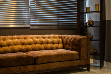 An elegant brown suede Chesterfield sofa sits in a modern office or living room. Light filters through horizontal blinds, creating a calm, sophisticated atmosphere.  © AlfRibeiro