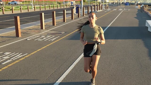 Young athletic woman with long dark hair jogging on a dedicated running and biking path in a park at sunset, demonstrating fitness and a healthy lifestyle. She is focused and determined