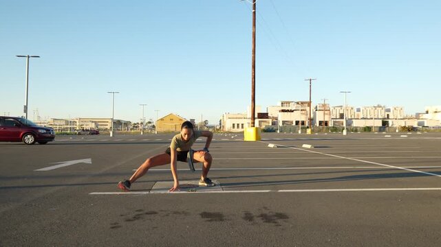 Young athletic woman performing warm-up exercises and stretching her legs in an empty urban parking lot before starting her morning run, getting ready for a cardio workout routine