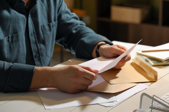 Man reading letter at wooden table indoors, closeup