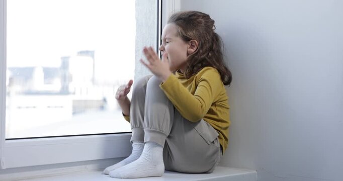 Autism. Little girl screaming on window sill indoors