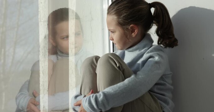 Autism. Little girl on window sill indoors