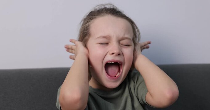 Autism. Little girl with sensory issues screaming on sofa indoors