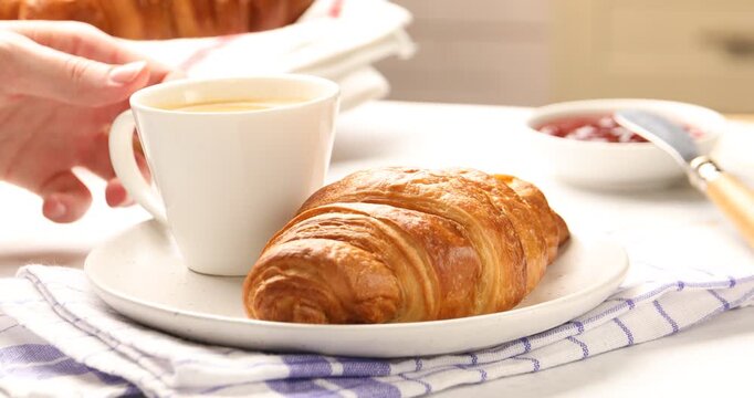 Puff pastry. Woman putting coffee near delicious croissant at white table, closeup