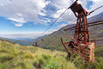 Fototapeta premium Rusty industrial mining structure and cables on a mountain slope overlooking a deep valley, historic mining site.