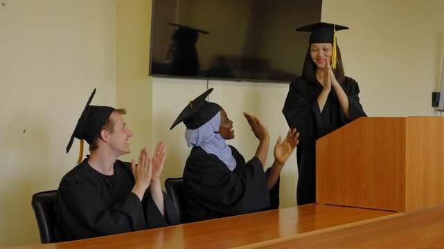 A young woman stands at the lectern and delivers a graduation speech to her classmates. 