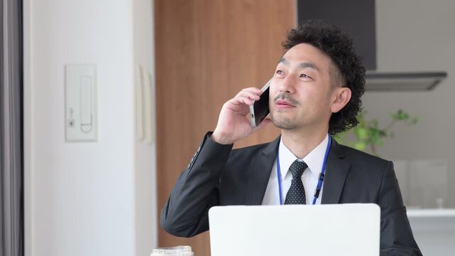 ノートパソコンを使いスマホで電話をするビジネスマンの髭の男性の動画