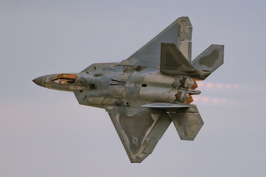 Lockheed Martin F-22 Raptor stealth fighter jet banking with afterburners in evening light