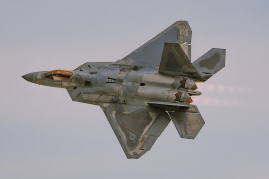 Lockheed Martin F-22 Raptor stealth fighter jet banking with afterburners in evening light
