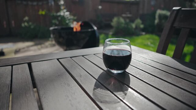 Red wine on a wooden table with a flaming BBQ in the background