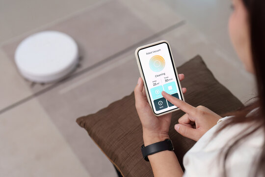Smart Home Cleaning. Woman controlling robotic vacuum through smartphone app.