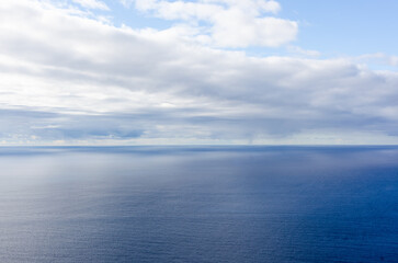 Fototapeta premium Atlantic Ocean view. Calm blue water stretches to the horizon. Low clouds hover above the sea. Scene photographed near Madeira, Portugal.
