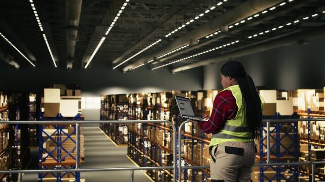 African American worker, shipping and delivery, process using laptop, warehouse facility. Managing logistics planning and supply chain control for package handling in busy fulfillment center.