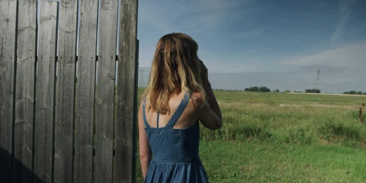 Woman gazing out over a field from a wooden fence