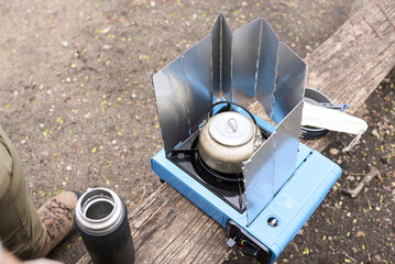 Unrecognizable person uses a windbreaker to be able to heat water on his camping gas stove even if it is windy. © Carolina Jaramillo