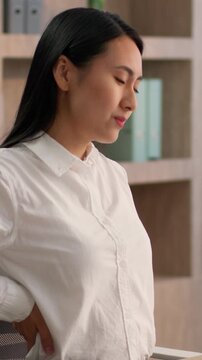 Tired Asian Chinese business woman suffering back pain massaging working laptop sick Japanese girl female businesswoman unhealthy Korean overworked worker computer sitting work ill backache in office