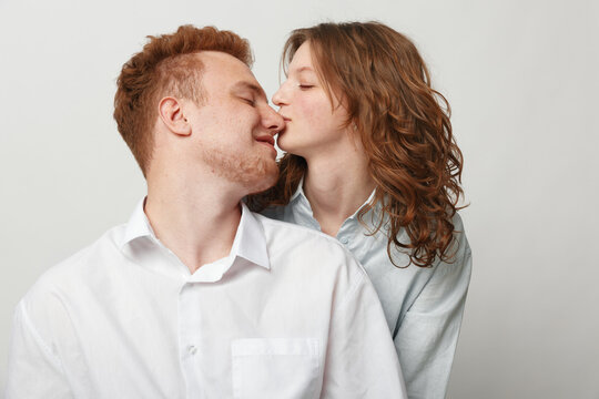 Young couple in casual clothes shares a tender moment with a gentle kiss on the nose. Intimate love and affection captured in a bright studio with a plain background.